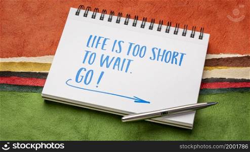Life is too short to wait. GO! Inspirational handwriting in a sketchbook against abstract paper landscape.