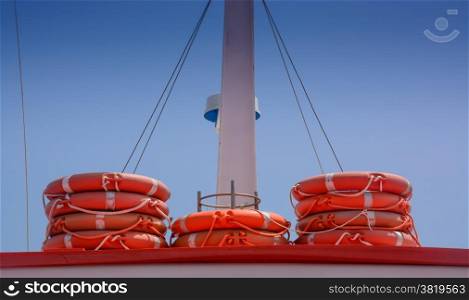 Life rings in orange color stacked on a boat with blue sky, ad space.