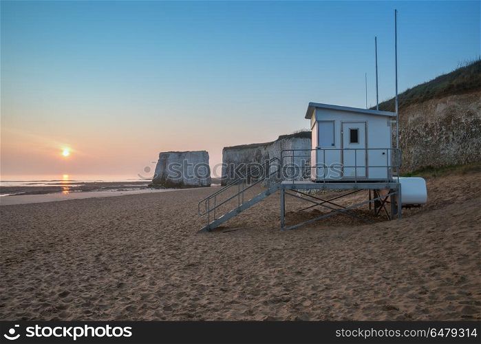 Lifeguard hut on empty beach during colorful sunrise with rock c. Lifeguard hut on empty beach during vibrant sunrise with rock cliffs in background