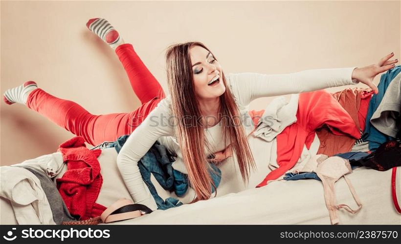 Lifestyle and decisions about outfit. Young female lie on sofa full of clothes. Woman with stretched arm try grab garment.. Woman lie on sofa full of clothes.