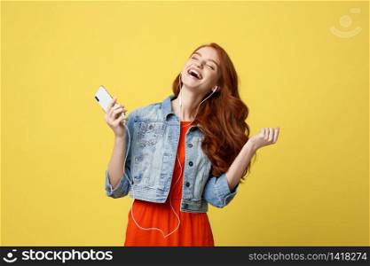 Lifestyle and Music Concept: Beautiful young curly red hair woman in headphones listening to music and dancing on vivid yellow background.. Lifestyle and Music Concept: Beautiful young curly red hair woman in headphones listening to music and dancing on vivid yellow background