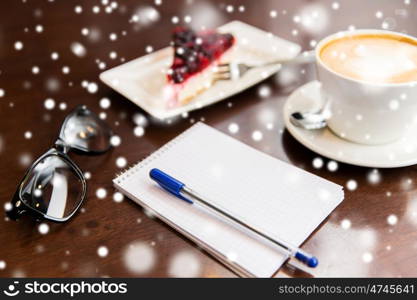 lifestyle and object concept - close up of notebook with pen, eyeglasses, coffee cup and berry cake on table over snow. close up of notebook with pen, coffee cup and cake