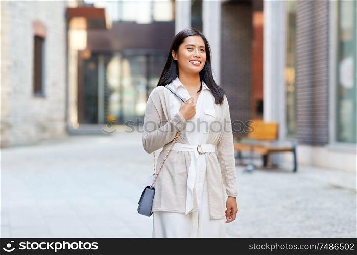 lifestyle and people concept - happy smiling young asian woman with handbag on city street. happy smiling young asian woman on city street