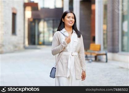 lifestyle and people concept - happy smiling young asian woman with handbag on city street. happy smiling young asian woman on city street