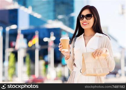 lifestyle and people concept - happy smiling young asian woman with takeaway coffee cup and lunch in paper bag on city street. happy woman with takeaway coffee and lunch in city