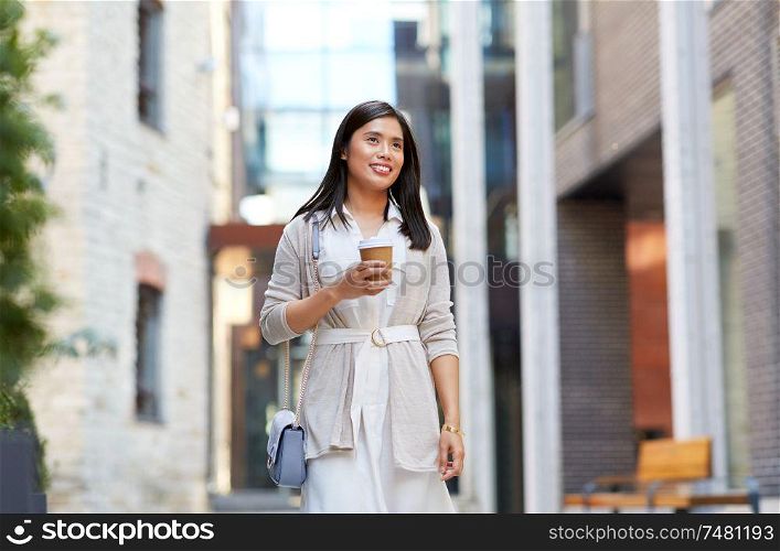 lifestyle and people concept - happy smiling young asian woman with takeaway coffee cup walking along city street. smiling woman with takeaway coffee cup in city