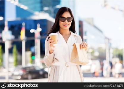 lifestyle and people concept - happy smiling young asian woman with takeaway coffee cup and lunch in paper bag on city street. happy woman with takeaway coffee and lunch in city