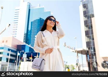 lifestyle and people concept - happy smiling young woman in sunglasses with handbag on city street. happy smiling young woman on city street