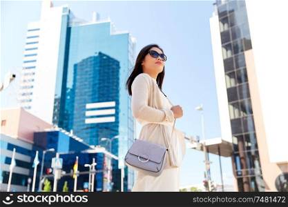 lifestyle and people concept - happy smiling young woman in sunglasses with handbag on city street. happy smiling young woman on city street