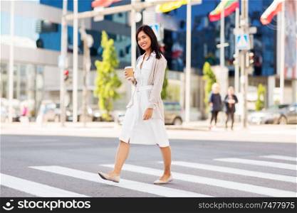 lifestyle and people concept - happy young asian woman with takeaway coffee cup walking along city street. asian woman with takeaway coffee cup in city