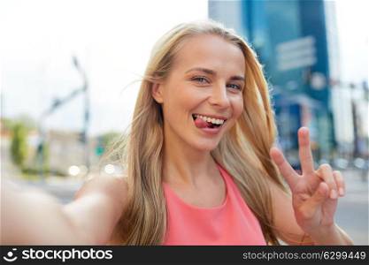 lifestyle and people concept - happy young woman taking selfie on city street and showing peace hand sign. happy young woman taking selfie on city street