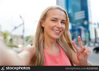 lifestyle and people concept - happy young woman taking selfie on city street and showing peace hand sign. happy young woman taking selfie on city street