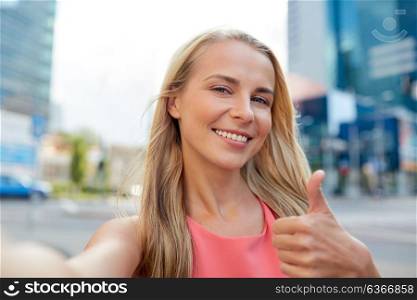 lifestyle and people concept - happy young woman taking selfie on city street and showing thumbs up. happy young woman taking selfie on city street