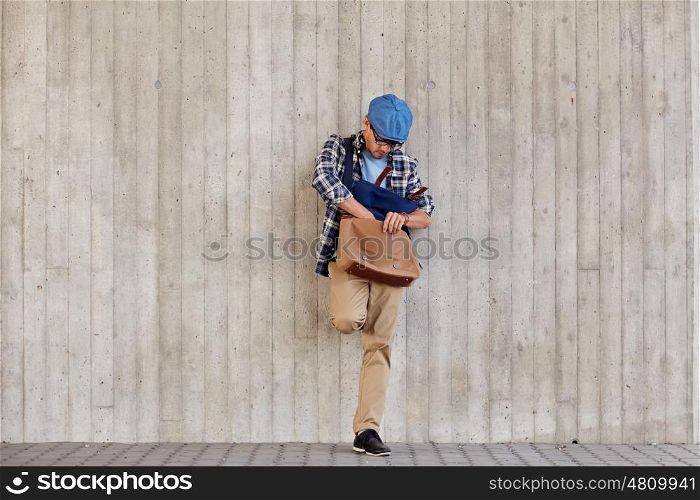 lifestyle and people concept - hipster man looking for something in his bag on city street. hipster man looking for something in his bag