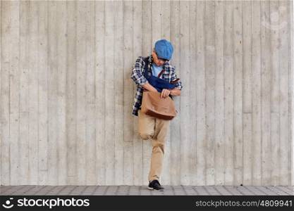lifestyle and people concept - hipster man looking for something in his bag on city street. hipster man looking for something in his bag