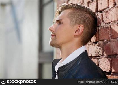 lifestyle and people concept - portrait of young man in leather jacket over brick wall outdoors. portrait of man in leather jacket over brick wall