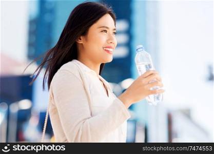 lifestyle and people concept - young asian woman drinking water flom plastic bottle in city. asian woman drinking water from bottle in city