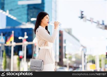 lifestyle and people concept - young asian woman drinking water flom plastic bottle in city. asian woman drinking water from bottle in city