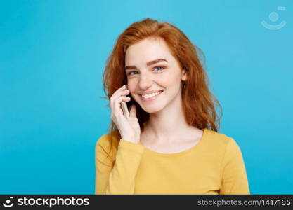 Lifestyle and Technology concept - Portrait of cheerful happy ginger red hair girl with joyful and exciting talking with friend by mobile phone. Isolated on Blue Pastel Background. Copy space.