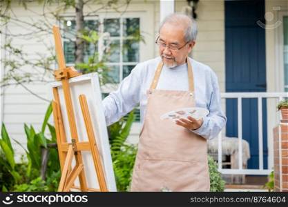Lifestyle Asian senior old man painting picture artwork using brush and oil color on canvas, elderly people smile paint at his easel outside green nature background, Happy retirement artist activity