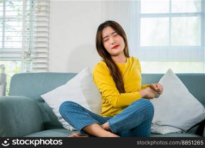 Lifestyle Asian young woman stretching her arms on sofa in the living room at home, happy female relaxing activity feeling lazy on weekend on couch, resting napping break