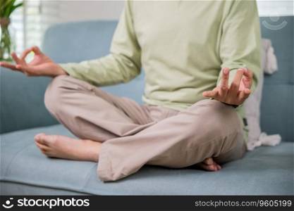 Lifestyle calm senior man lotus pose doing yoga for mental balance breathing air relaxing on sofa at home, Asian elderly old man sitting practise yoga and meditation in lotus position and closed eyes