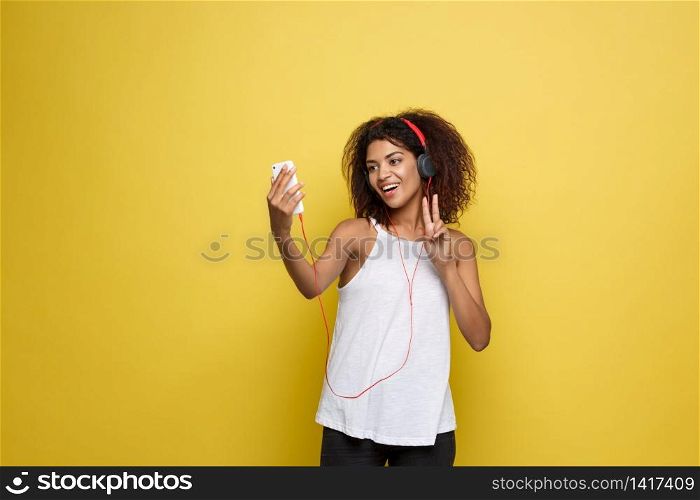 Lifestyle Concept - Portrait of beautiful African American woman joyful listening to music and take a photo on mobile phone. Yellow pastel studio background. Copy Space.. Lifestyle Concept - Portrait of beautiful African American woman joyful listening to music and take a photo on mobile phone. Yellow pastel studio background. Copy Space