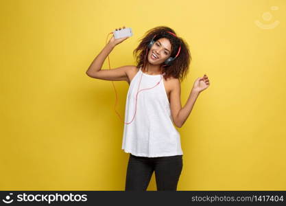 Lifestyle Concept - Portrait of beautiful African American woman joyful listening to music on mobile phone. Yellow pastel studio background. Copy Space.. Lifestyle Concept - Portrait of beautiful African American woman joyful listening to music on mobile phone. Yellow pastel studio background. Copy Space