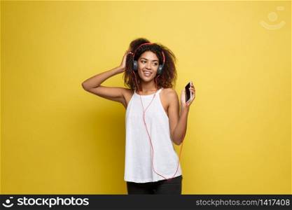 Lifestyle Concept - Portrait of beautiful African American woman joyful listening to music on mobile phone. Yellow pastel studio background. Copy Space.. Lifestyle Concept - Portrait of beautiful African American woman joyful listening to music on mobile phone. Yellow pastel studio background. Copy Space