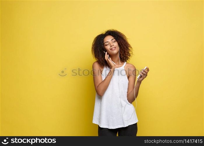 Lifestyle Concept - Portrait of beautiful African American woman joyful listening to music on mobile phone. Yellow pastel studio background. Copy Space. Lifestyle Concept - Portrait of beautiful African American woman joyful listening to music on mobile phone. Yellow pastel studio background. Copy Space.