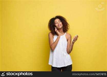 Lifestyle Concept - Portrait of beautiful African American woman joyful listening to music on mobile phone. Yellow pastel studio background. Copy Space. Lifestyle Concept - Portrait of beautiful African American woman joyful listening to music on mobile phone. Yellow pastel studio background. Copy Space.