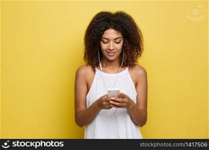 Lifestyle Concept - Portrait of beautiful African American woman joyful listening to music on mobile phone. Yellow pastel studio background. Copy Space.. Lifestyle Concept - Portrait of beautiful African American woman joyful listening to music on mobile phone. Yellow pastel studio background. Copy Space