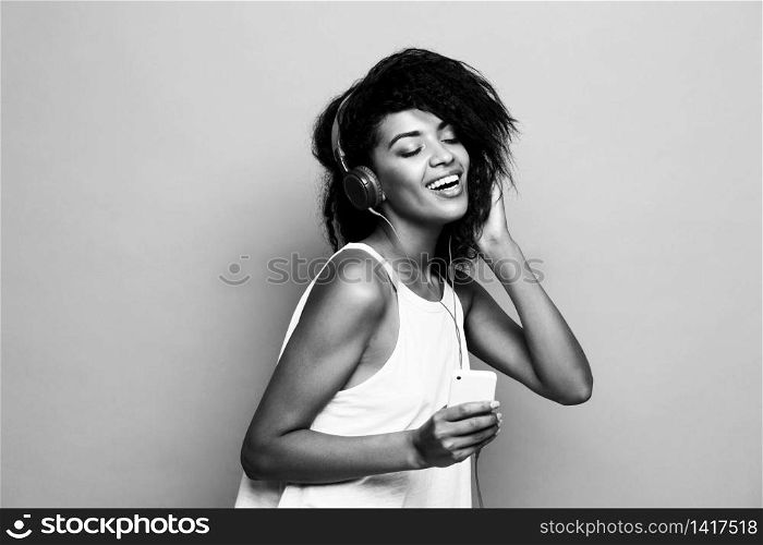 Lifestyle Concept - Portrait of beautiful African American woman joyful listening to music on mobile phone. Yellow pastel studio background. Black and white. Lifestyle Concept - Portrait of beautiful African American woman joyful listening to music on mobile phone. Yellow pastel studio background. Black and white.