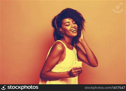 Lifestyle Concept - Portrait of beautiful African American woman joyful listening to music on mobile phone. Yellow pastel studio background. Copy Space.. Lifestyle Concept - Portrait of beautiful African American woman joyful listening to music on mobile phone. pastel studio background. Copy Space