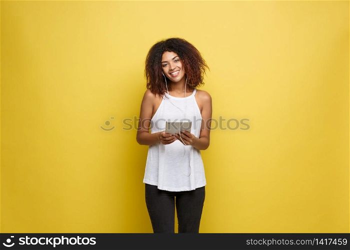 Lifestyle Concept - Portrait of beautiful African American woman joyful listening to music on tablet. Yellow pastel studio background. Copy Space. Lifestyle Concept - Portrait of beautiful African American woman joyful listening to music on tablet. Yellow pastel studio background. Copy Space.