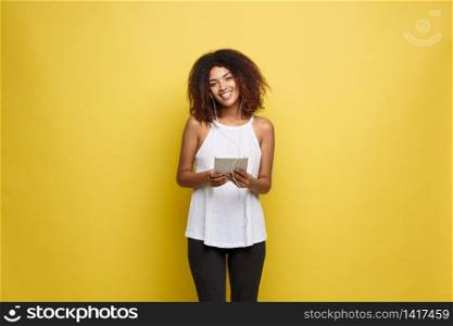 Lifestyle Concept - Portrait of beautiful African American woman joyful listening to music on tablet. Yellow pastel studio background. Copy Space. Lifestyle Concept - Portrait of beautiful African American woman joyful listening to music on tablet. Yellow pastel studio background. Copy Space.