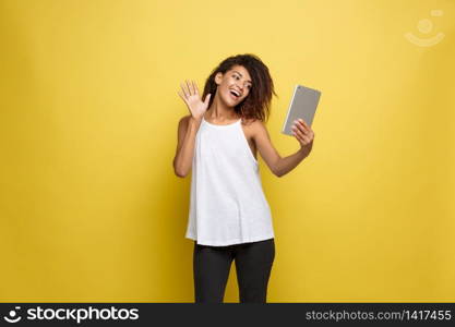 Lifestyle Concept - Portrait of beautiful African American woman joyful playing something on electronic tablet. Yellow pastel studio background. Copy Space. Lifestyle Concept - Portrait of beautiful African American woman joyful playing something on electronic tablet. Yellow pastel studio background. Copy Space.