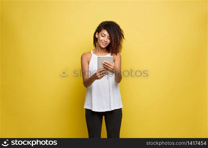 Lifestyle Concept - Portrait of beautiful African American woman joyful reading something on electronic tablet. Yellow pastel studio background. Copy Space. Lifestyle Concept - Portrait of beautiful African American woman joyful reading something on electronic tablet. Yellow pastel studio background. Copy Space.