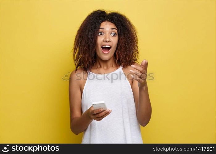 Lifestyle Concept - Portrait of beautiful African American woman shocking see someone and holding mobile phone. Yellow pastel studio background. Copy Space. Lifestyle Concept - Portrait of beautiful African American woman shocking see someone and holding mobile phone. Yellow pastel studio background. Copy Space.