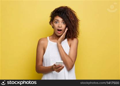 Lifestyle Concept - Portrait of beautiful African American woman shocking with something on mobile phone. Yellow pastel studio background. Copy Space. Lifestyle Concept - Portrait of beautiful African American woman shocking with something on mobile phone. Yellow pastel studio background. Copy Space.