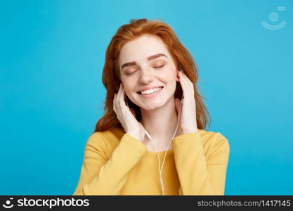 Lifestyle concept - Portrait of cheerful happy ginger red hair girl enjoy listening to music with headphones joyful smiling to camera. Isolated on Blue Pastel Background. Copy space.