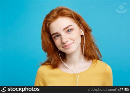Lifestyle concept - Portrait of cheerful happy ginger red hair girl enjoy listening to music with headphones joyful smiling to camera. Isolated on Blue Pastel Background. Copy space.