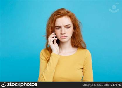 Lifestyle concept - Portrait of ginger red hair girl with shocking and stressful expression while talking with friend by mobile phone. Isolated on Blue Pastel Background. Copy space.