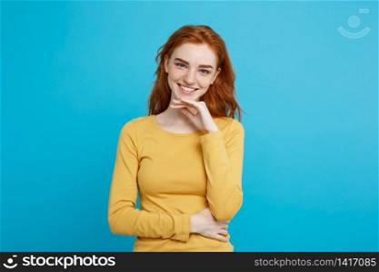 Lifestyle concept - Portrait of young stylish freckled girl laughing with hand on chin looking at camera. Blue Pastel Background. Copy space.