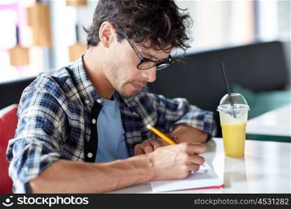 lifestyle, creativity, freelance, inspiration and people concept - creative man with notebook or diary writing and drinking juice at cafe