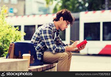 lifestyle, creativity, freelance, inspiration and people concept - creative man with notebook or diary writing sitting on city street bench. man with notebook or diary writing on city street