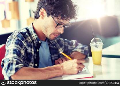 lifestyle, creativity, freelance, inspiration and people concept - creative man with notebook or diary writing and drinking juice at cafe. man with notebook and juice writing at cafe