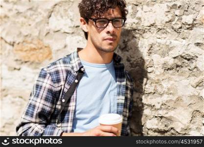 lifestyle, drinks and people concept - man in eyeglasses drinking coffee from disposable paper cup over street wall