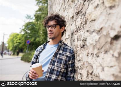 lifestyle, drinks and people concept - man in eyeglasses drinking coffee from disposable paper cup over stone street wall
