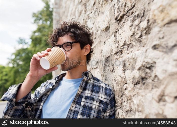lifestyle, drinks and people concept - man in eyeglasses drinking coffee from disposable paper cup over stone street wall